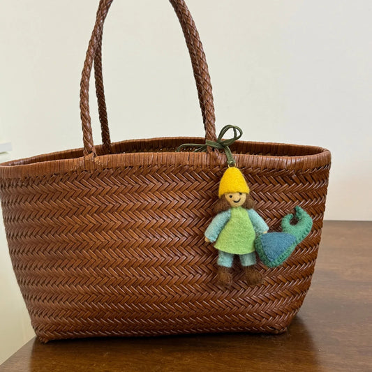 Handmade wool felt girl and beetle bag charm displayed on a woven tote