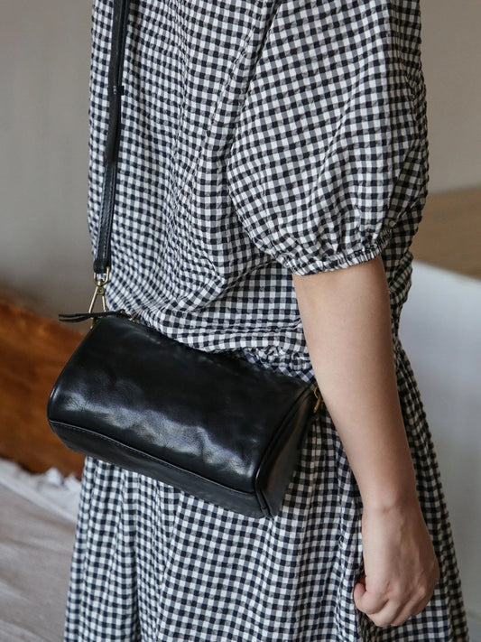 Black vegetable-tanned leather barrel crossbody bag worn over the shoulder