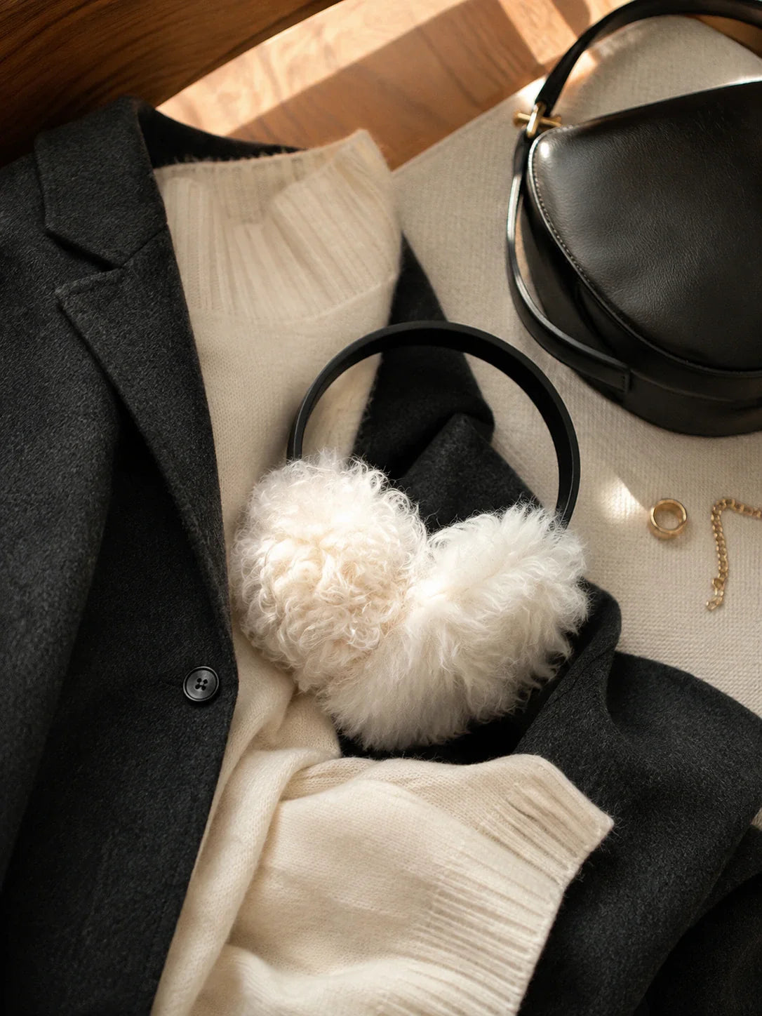 White wool earmuffs with a black headband styled with black and cream winter layers