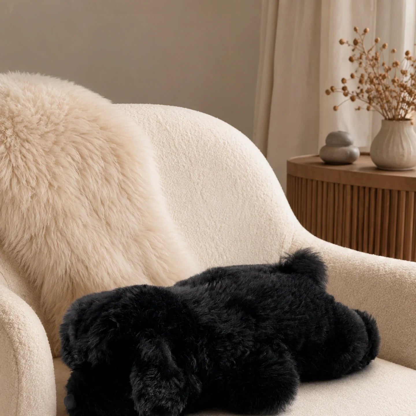 Black lambswool poodle pillow on a cream lounge chair