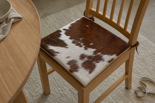 Forty-centimeter square cowhide tie-on pad centered on a wooden dining chair with seat edges visible