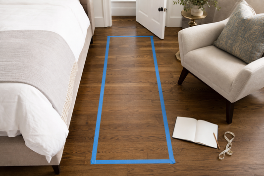 Painter-tape rug footprint measured between a bed and lounge chair