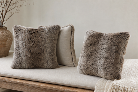 Single-sided and double-sided rabbit fur pillows shown from front and reverse on a neutral bench