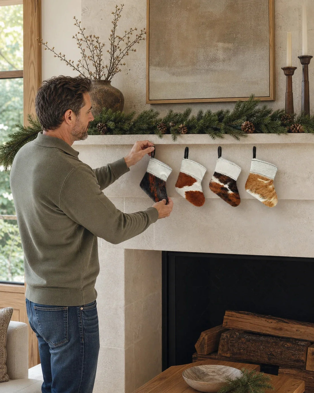 Capricornus Living Four-piece cowhide holiday stocking ornament set being installed on an American fireplace mantel