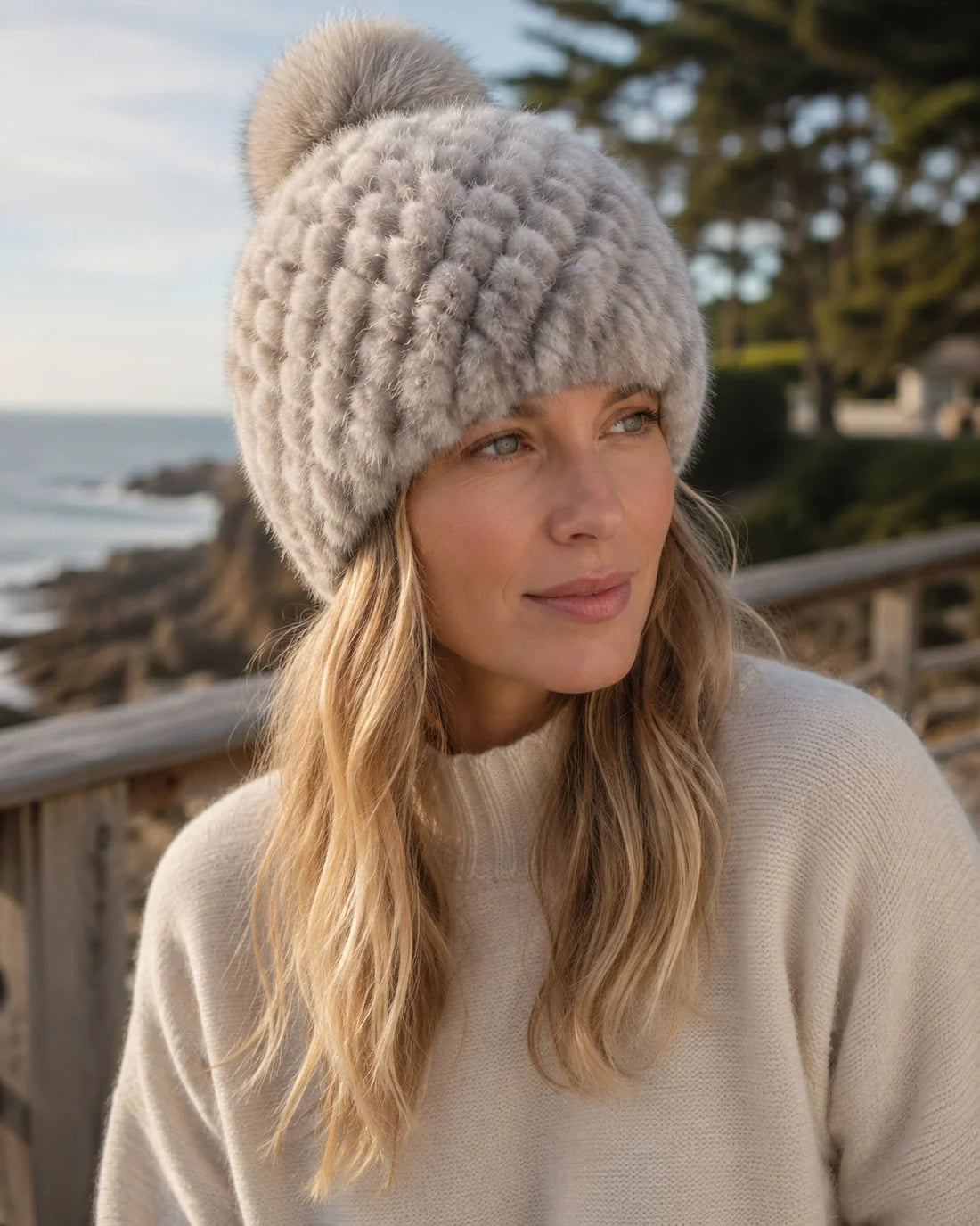 Silver gray genuine mink fur knitted beanie with fox fur pom-pom worn on a cold coastal walk