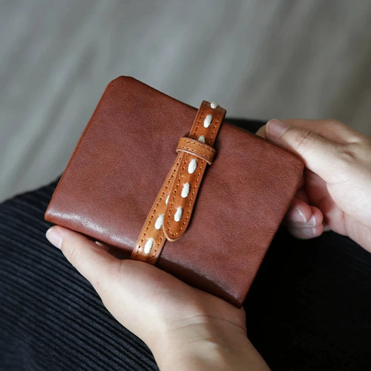Brown vegetable-tanned leather bifold wallet with contrast strap closure