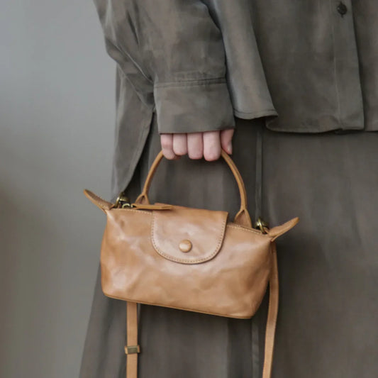 Chestnut brown vegetable-tanned leather mini crossbody bag carried by the top handle