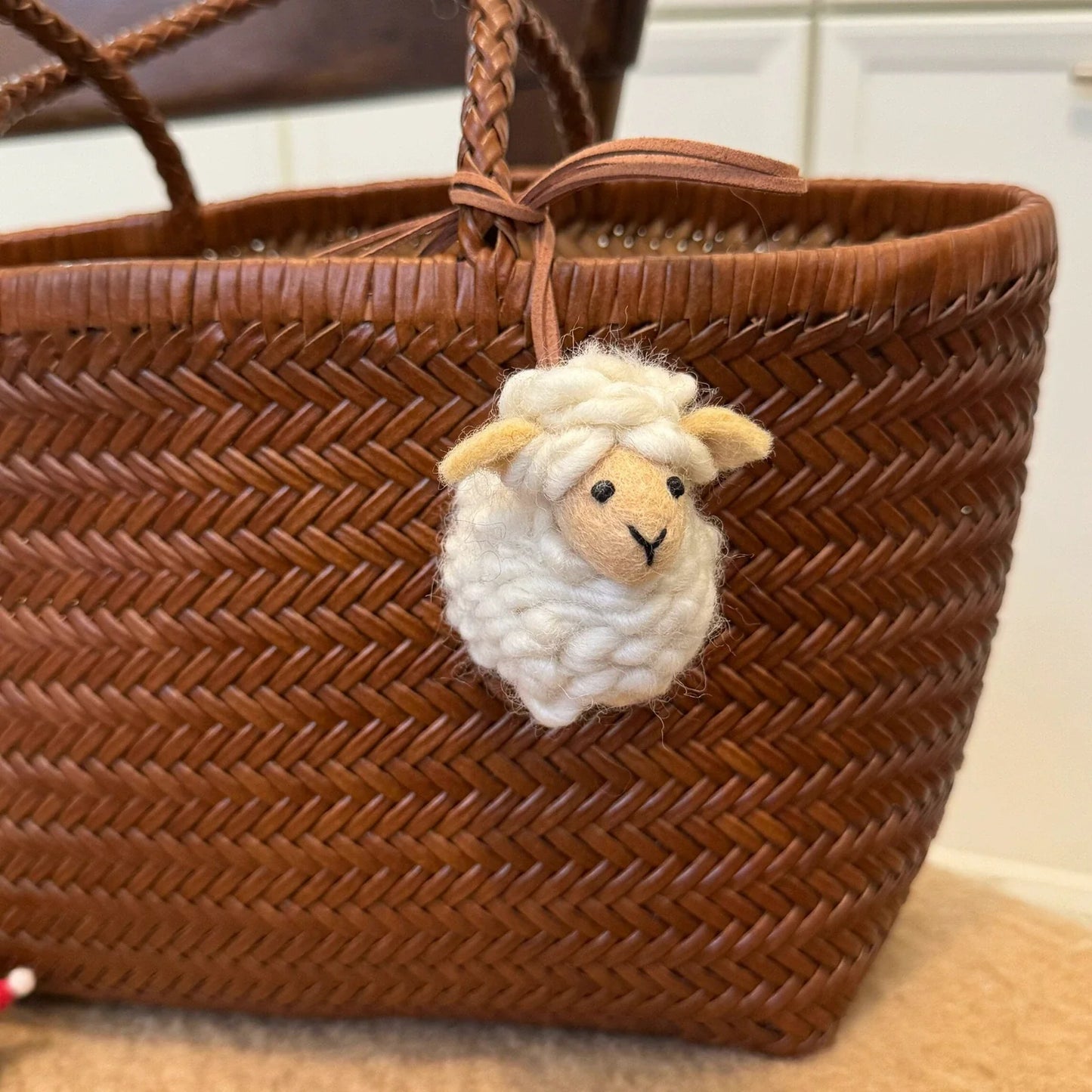 Cream handmade wool felt sheep bag charm displayed on a woven basket