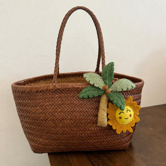 Handmade wool felt palm tree and smiling sun bag charm on woven basket