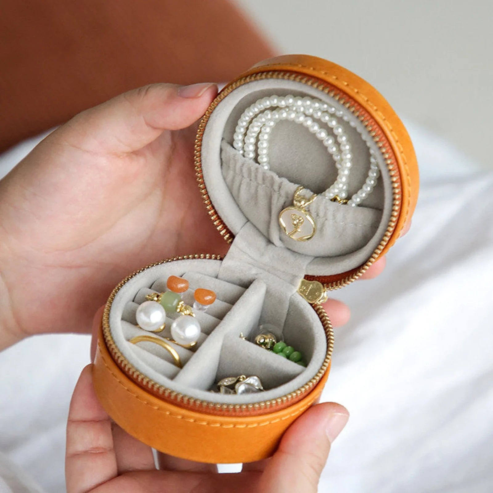 Open round vegetable-tanned leather travel jewelry case with organized rings, earrings, and necklace
