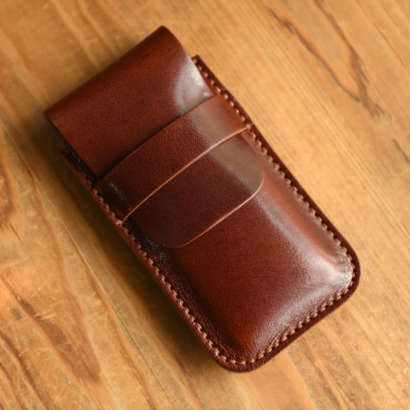 Hand-stitched brown leather travel watch pouch on a warm wood surface