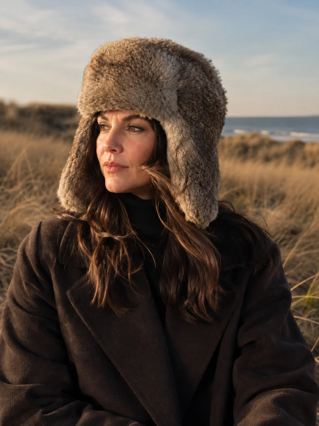 Woman wearing a taupe rabbit fur trapper hat in a winter coastal setting