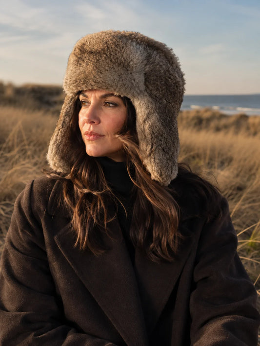 Woman wearing a taupe rabbit fur trapper hat in a winter coastal setting