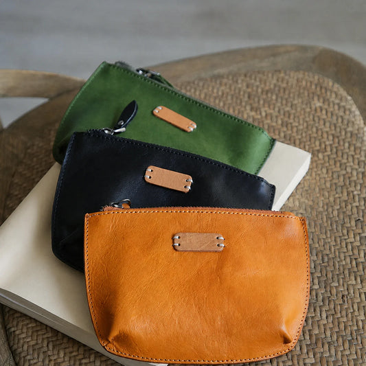 Three vegetable-tanned top-grain leather cosmetic pouches in black, sunset yellow, and matcha green