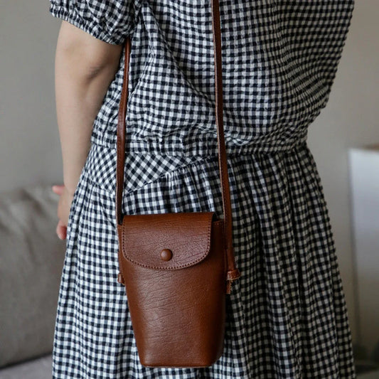 Women's brown leather phone crossbody bag worn over a checked dress