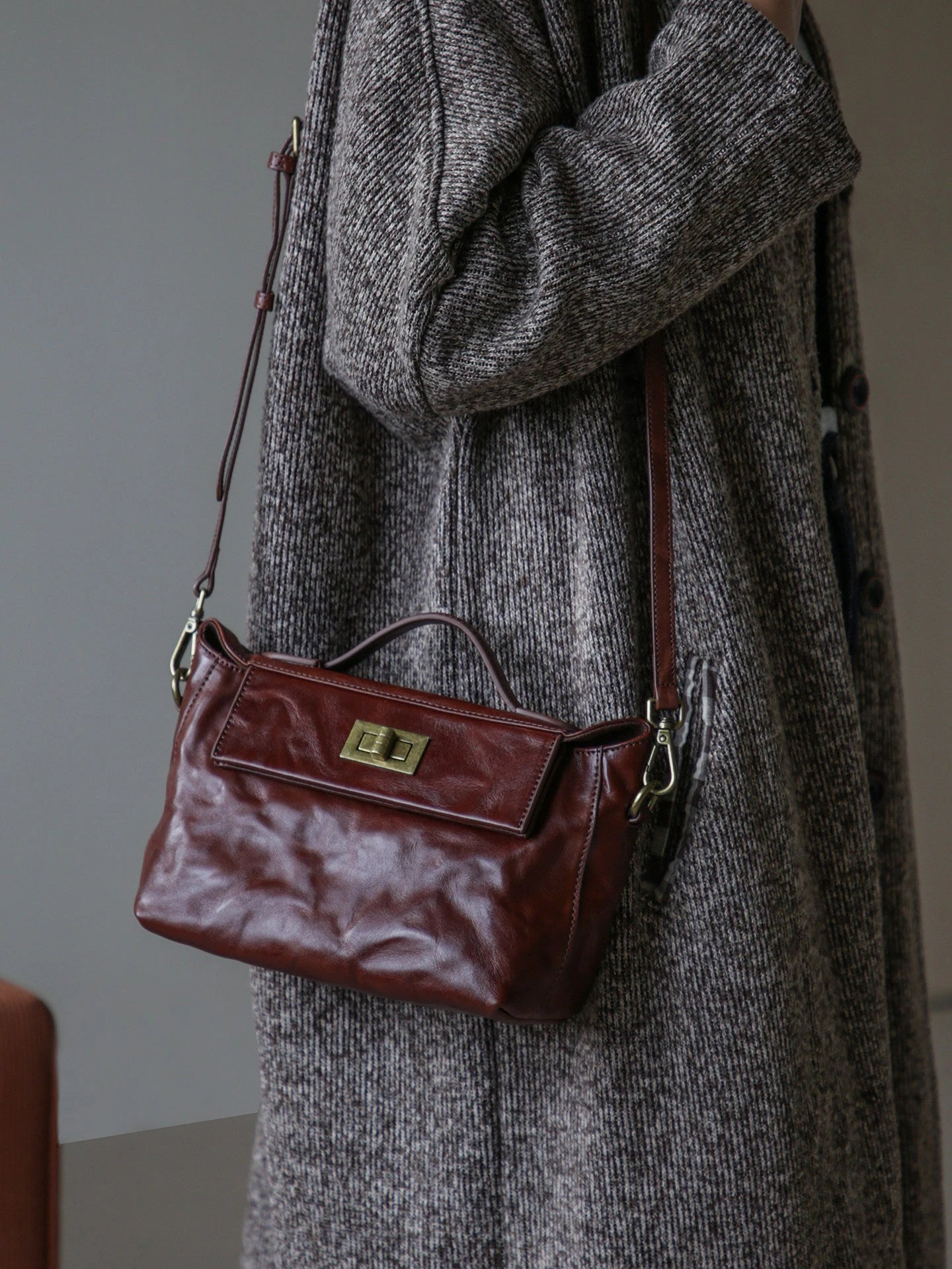 Chestnut brown leather satchel worn with its adjustable shoulder strap