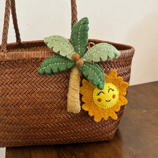 Close view of handmade wool felt palm tree and smiling sun bag charms