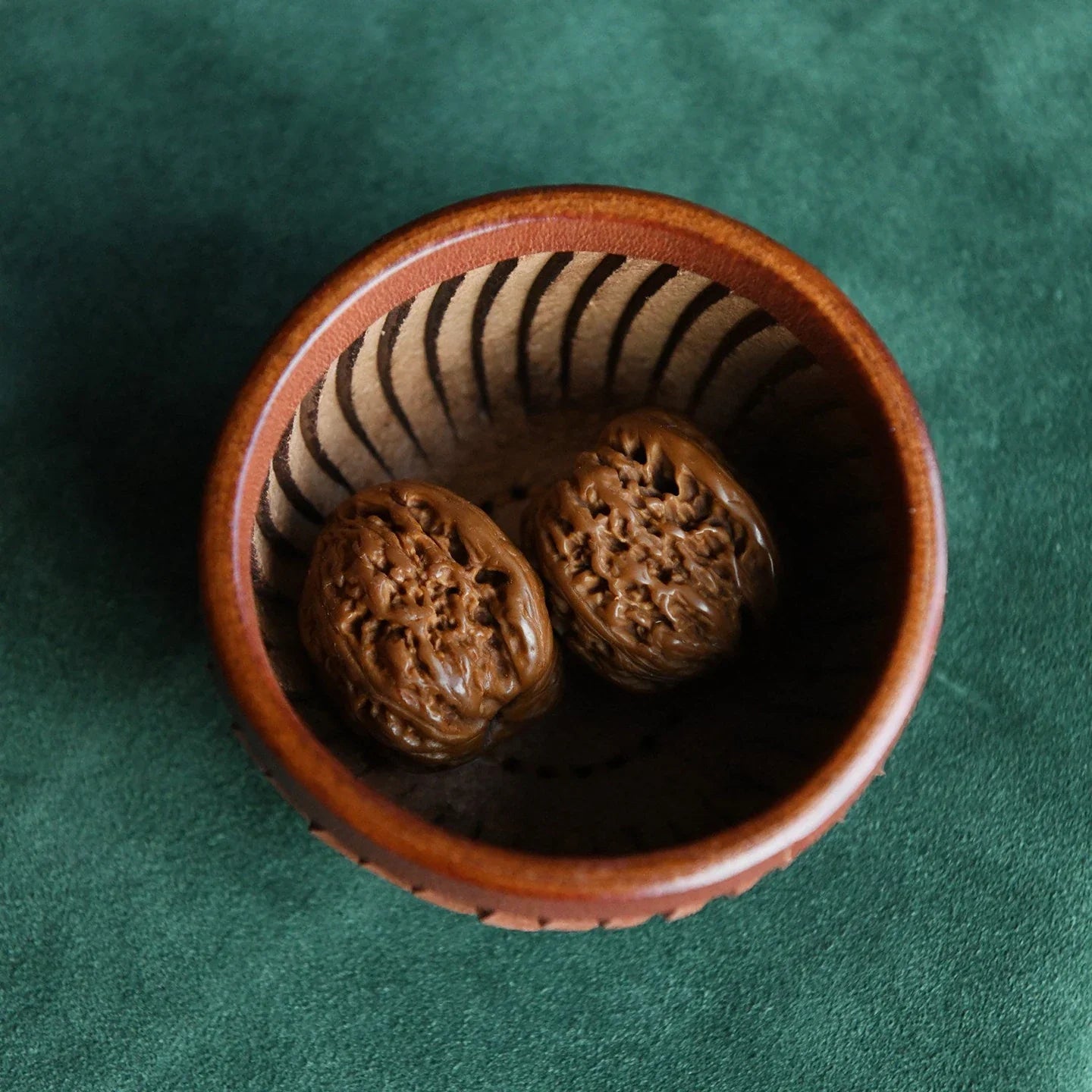 Round leather catchall bowl holding walnuts on a green surface
