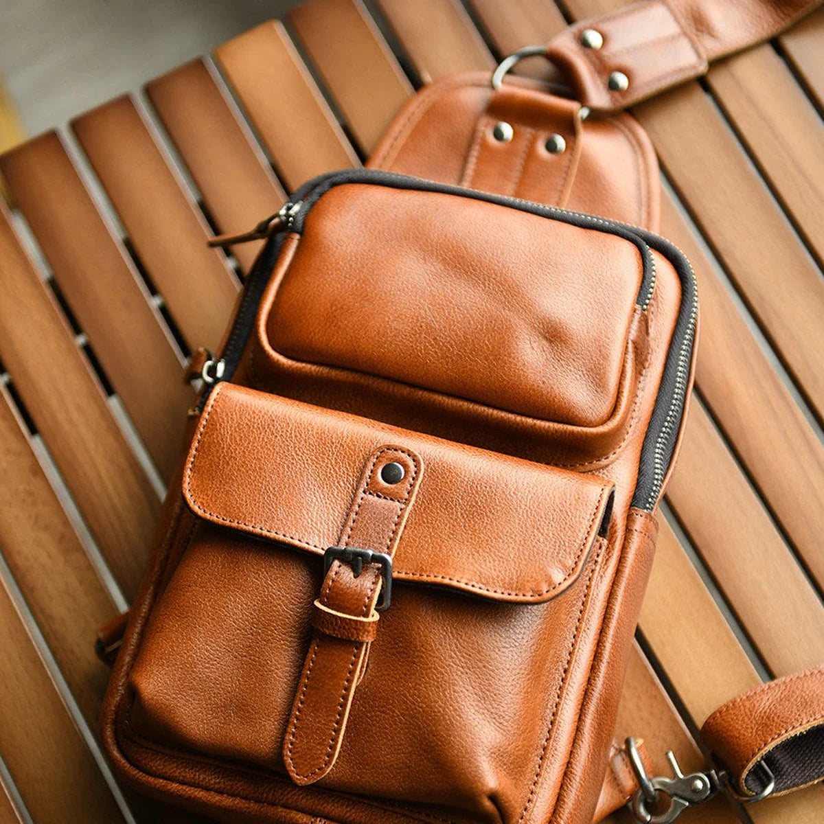 Brown leather sling bag front pockets, buckle, and zipper detail