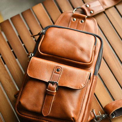 Brown leather sling bag front pockets, buckle, and zipper detail