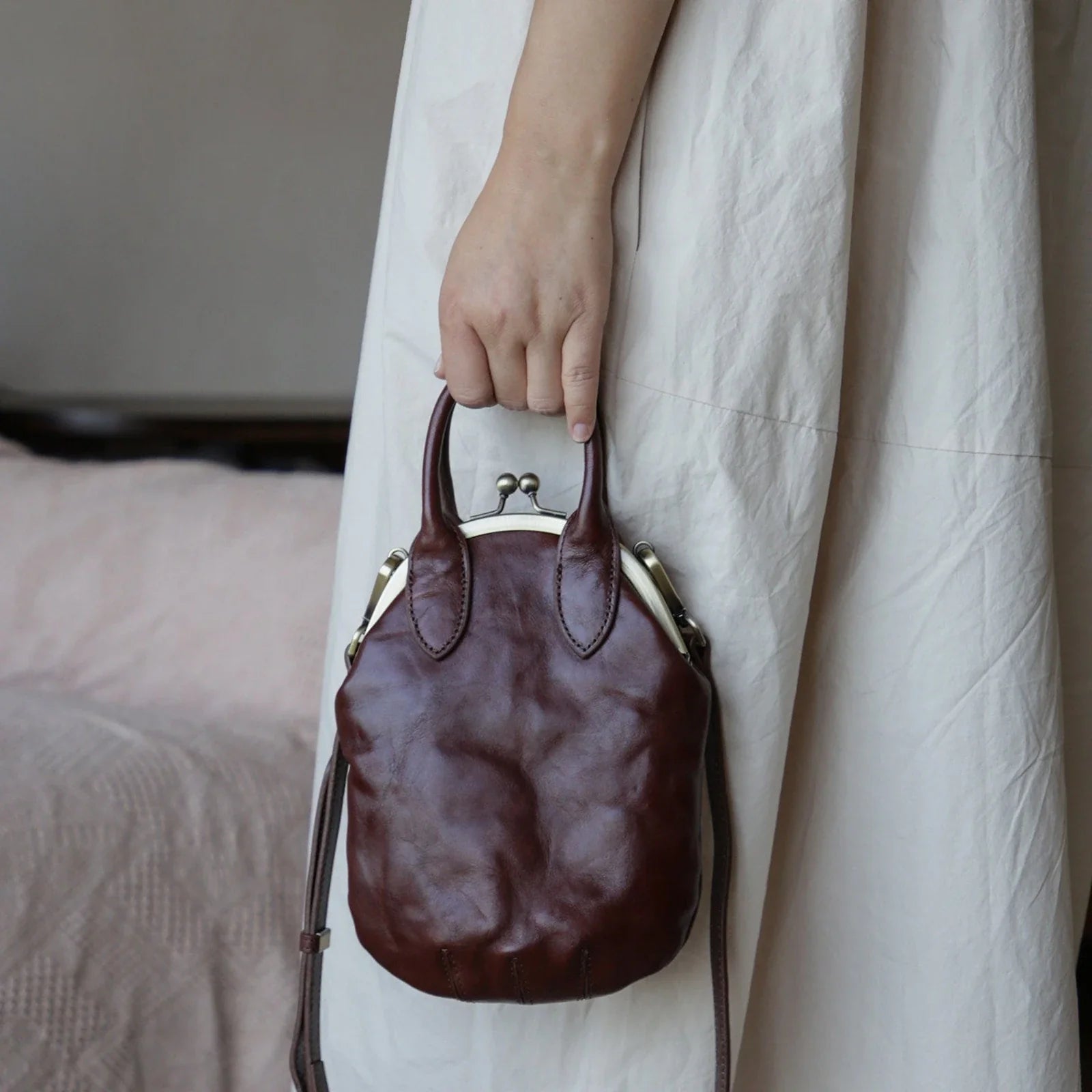 Brown vintage leather kiss-lock phone bag carried by the top handles