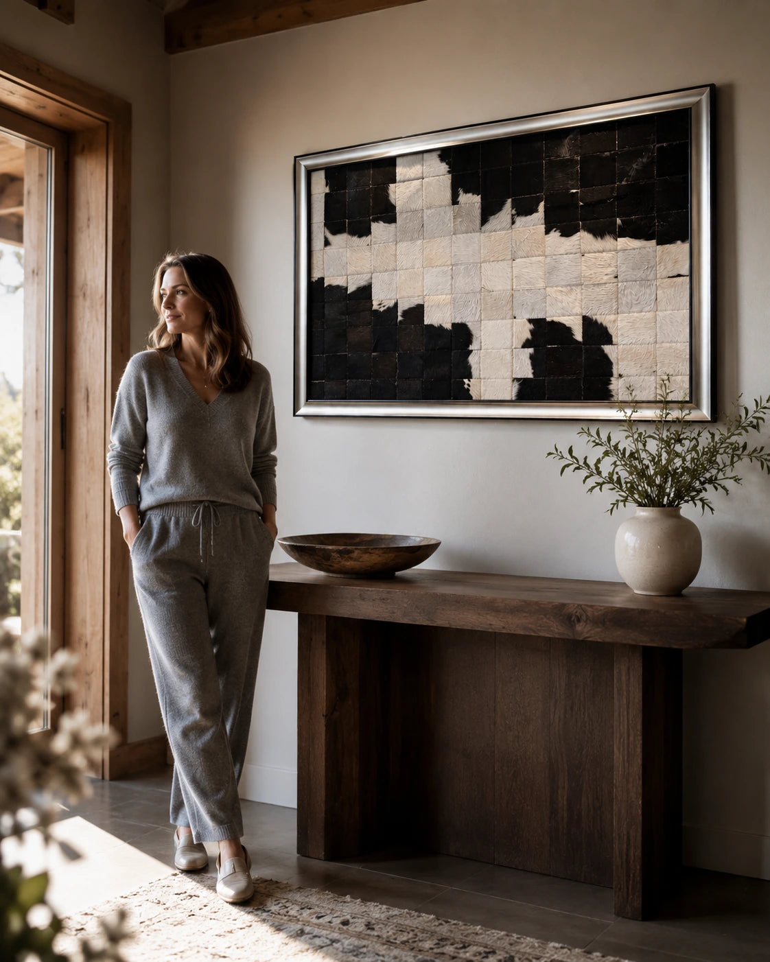 Woman standing beside black and ivory framed cowhide patchwork wall art above a wood console