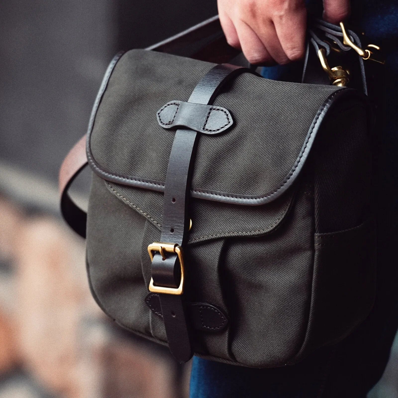 Olive green waxed canvas and leather messenger bag carried by its top handle