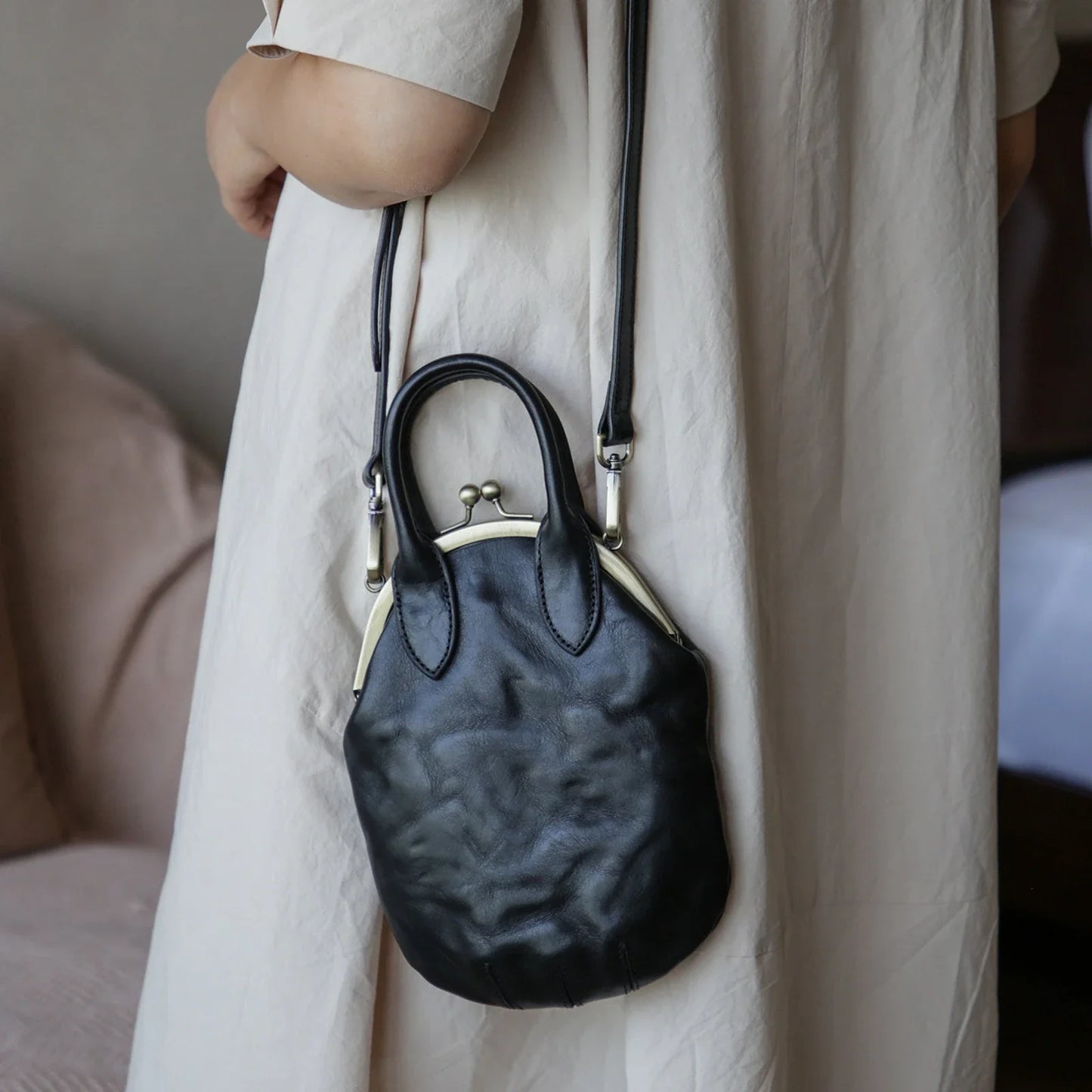 Black kiss-lock leather crossbody phone bag worn at the side