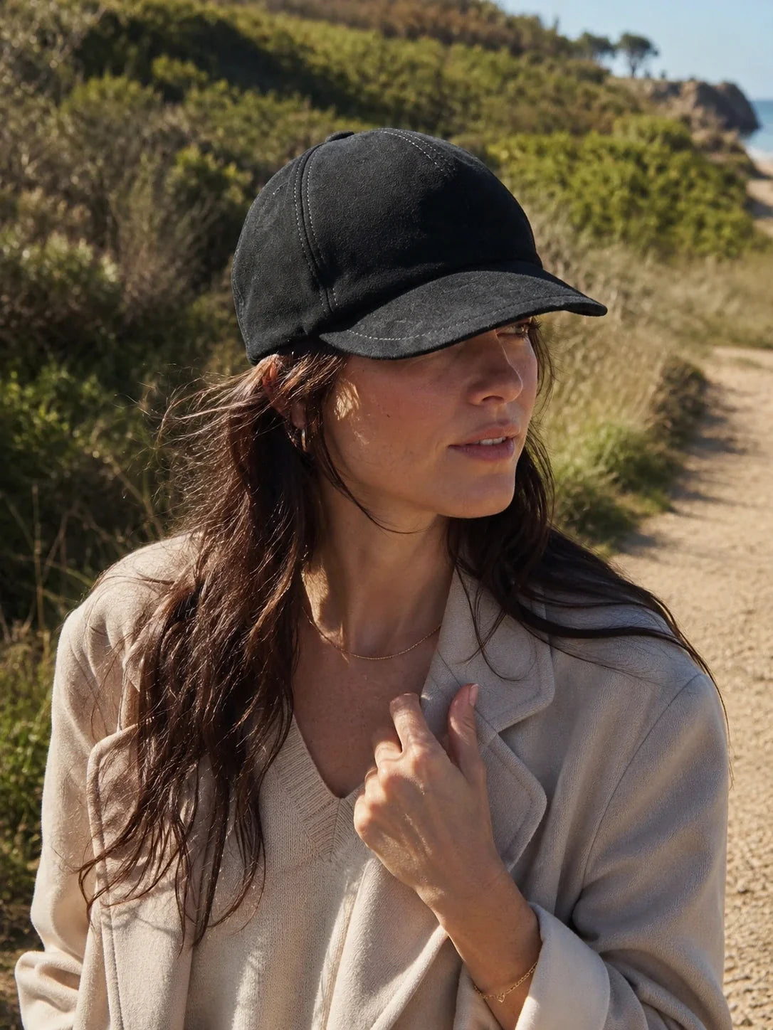 Woman styling a black suede lambskin beret cap on a coastal walk