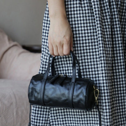 Black vegetable-tanned leather mini barrel bag carried by hand