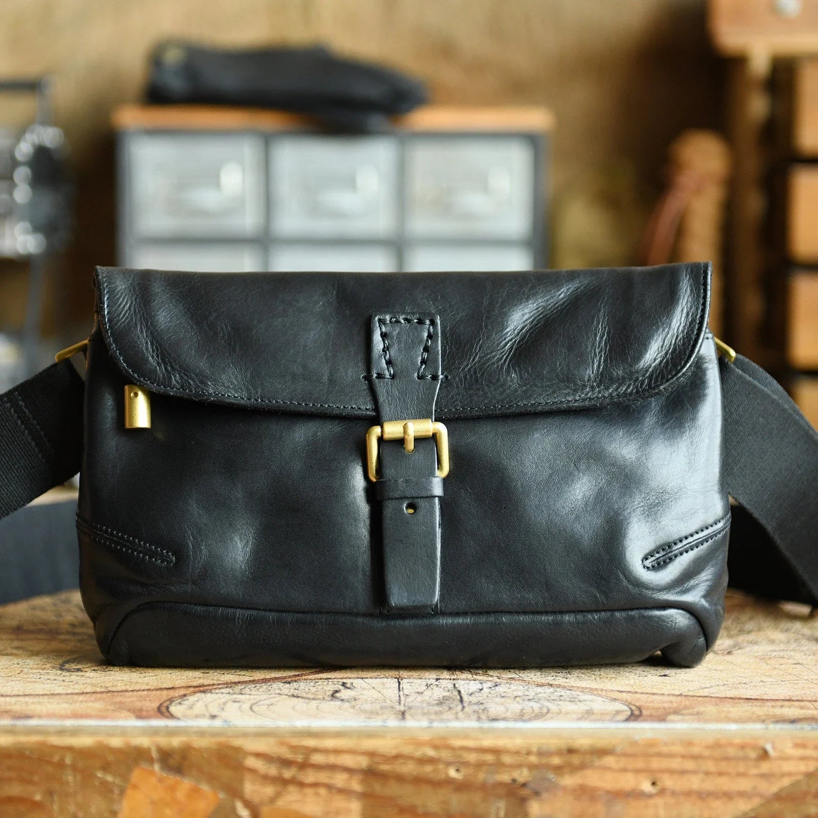 Black vegetable-tanned cowhide messenger bag leather grain and brass-tone buckle detail