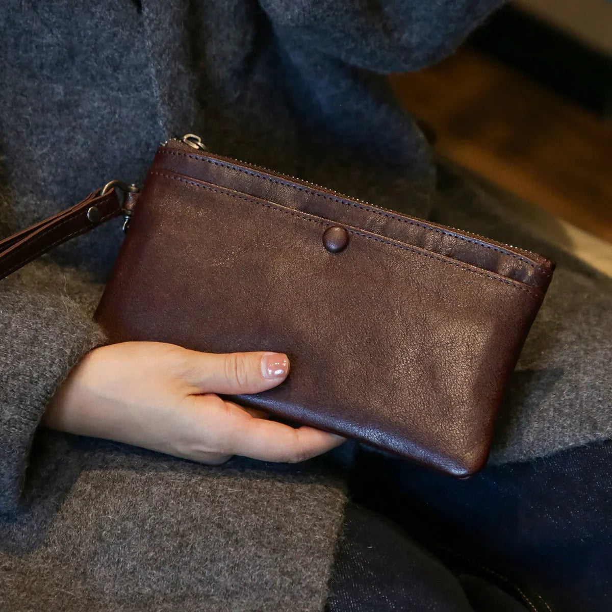Coffee brown leather long wallet held against a grey knit