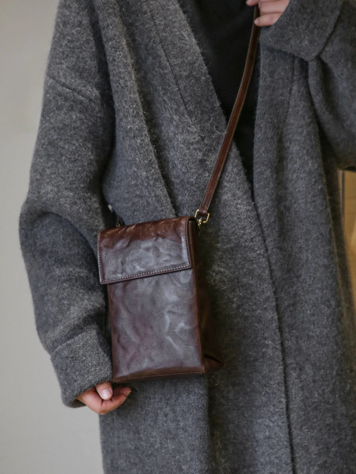 Deep brown leather phone crossbody bag worn over a wool coat