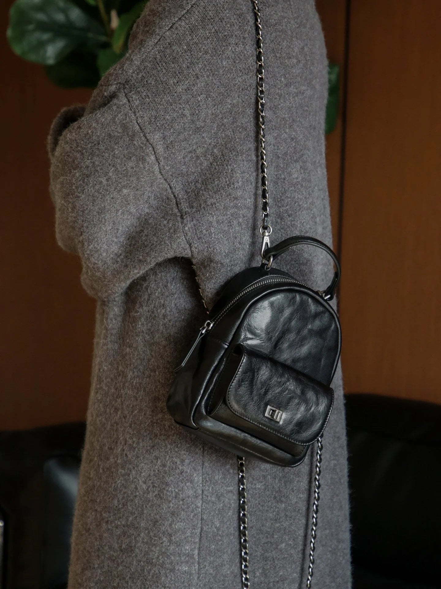 Black vegetable-tanned leather mini backpack styled over a grey coat