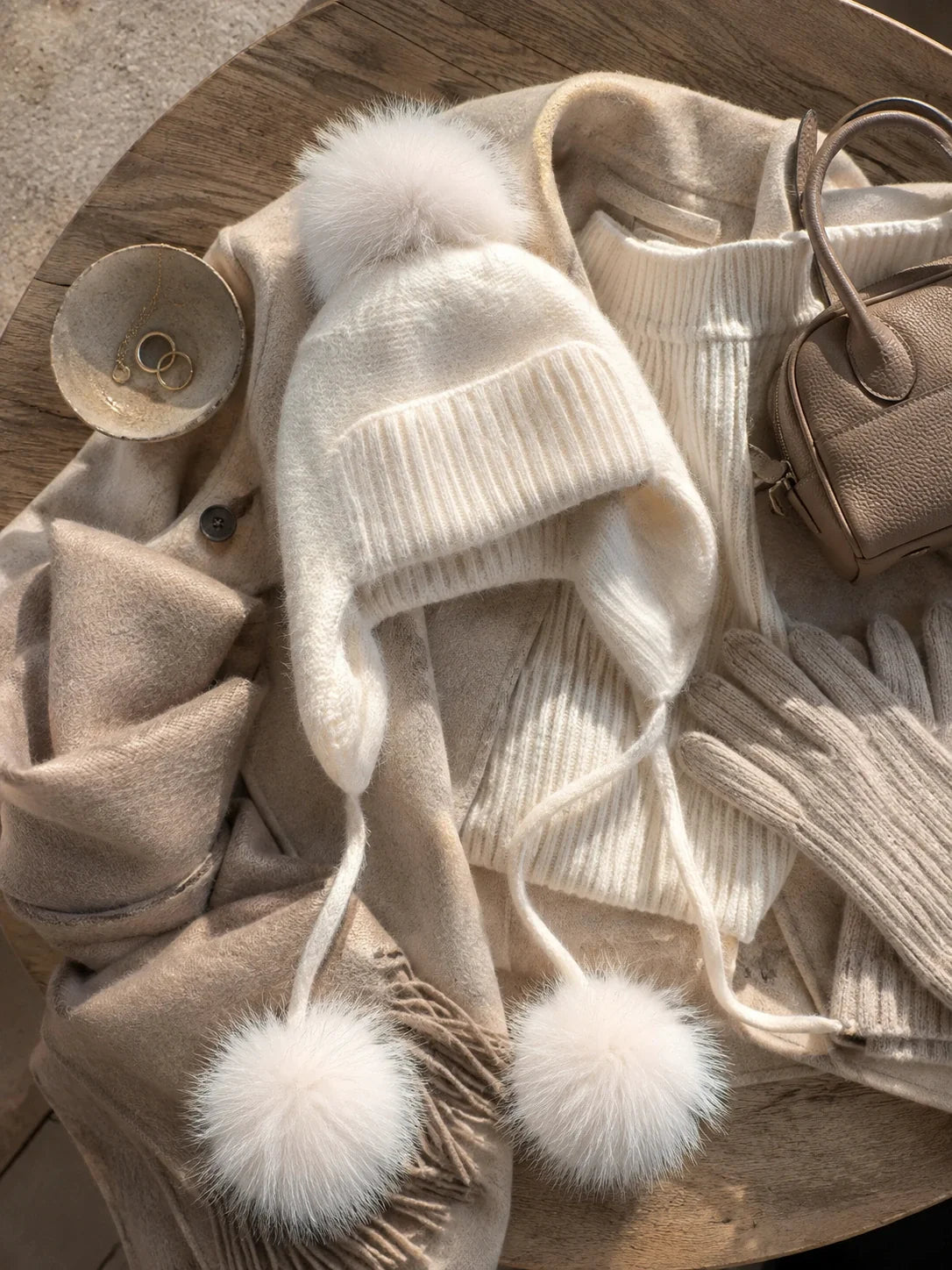 White knit earflap pom-pom hat styled with neutral winter layers