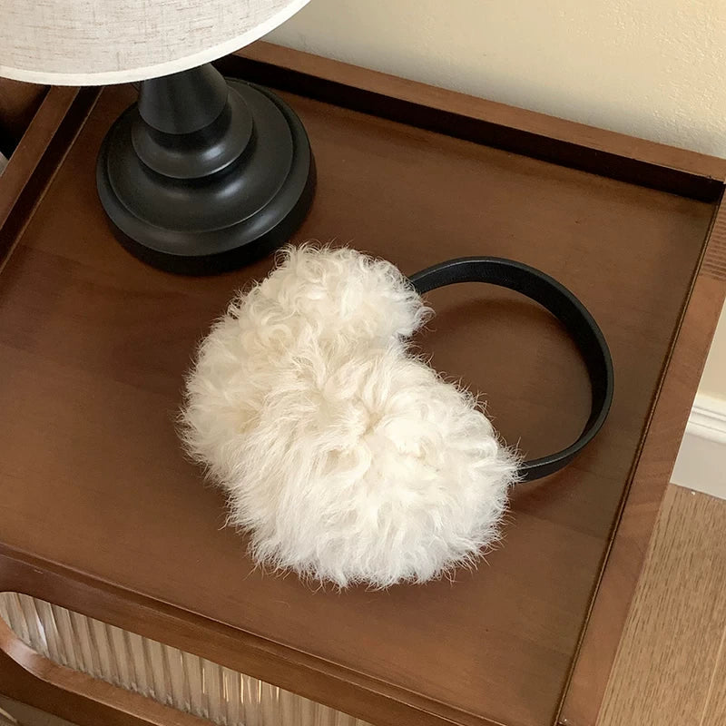 White wool earmuffs with a black headband displayed on a wooden table