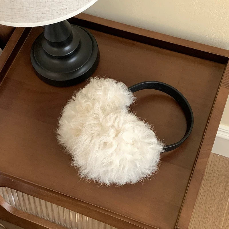 White wool earmuffs with a black headband displayed on a wooden table