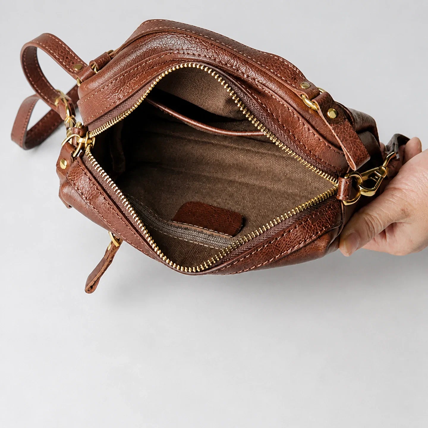 Open brown leather crossbody bag showing cotton lining and interior zipper pocket