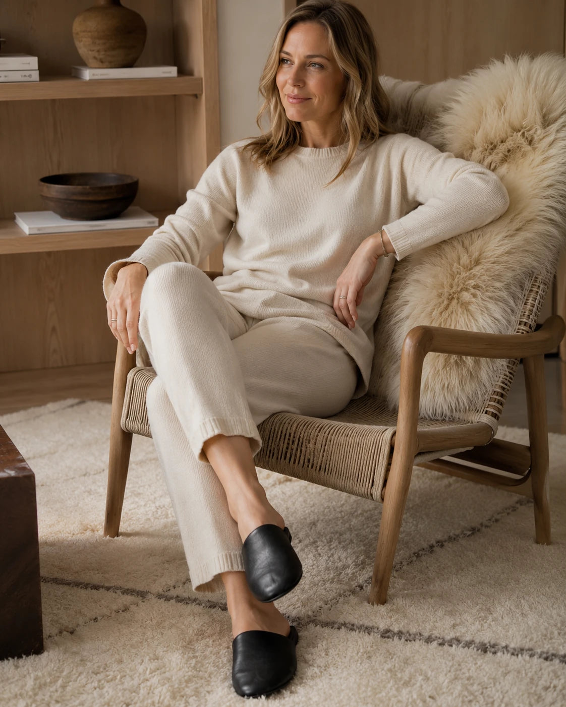 Woman wearing black lambskin travel slippers beside a hotel chair