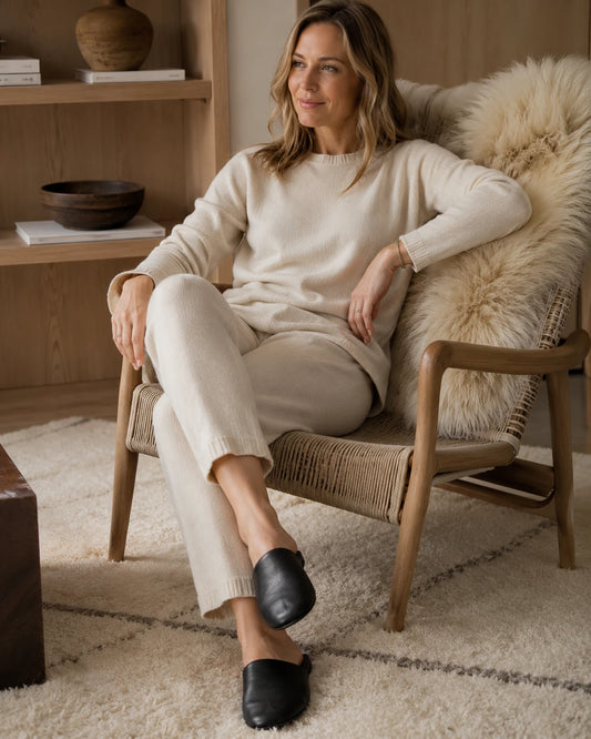 Woman wearing black lambskin travel slippers beside a hotel chair