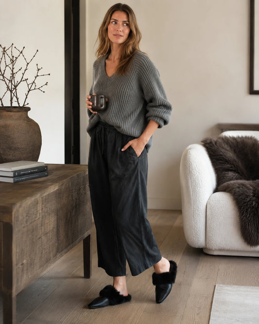 Woman wearing black cowhide and rabbit fur mule slippers in a living room