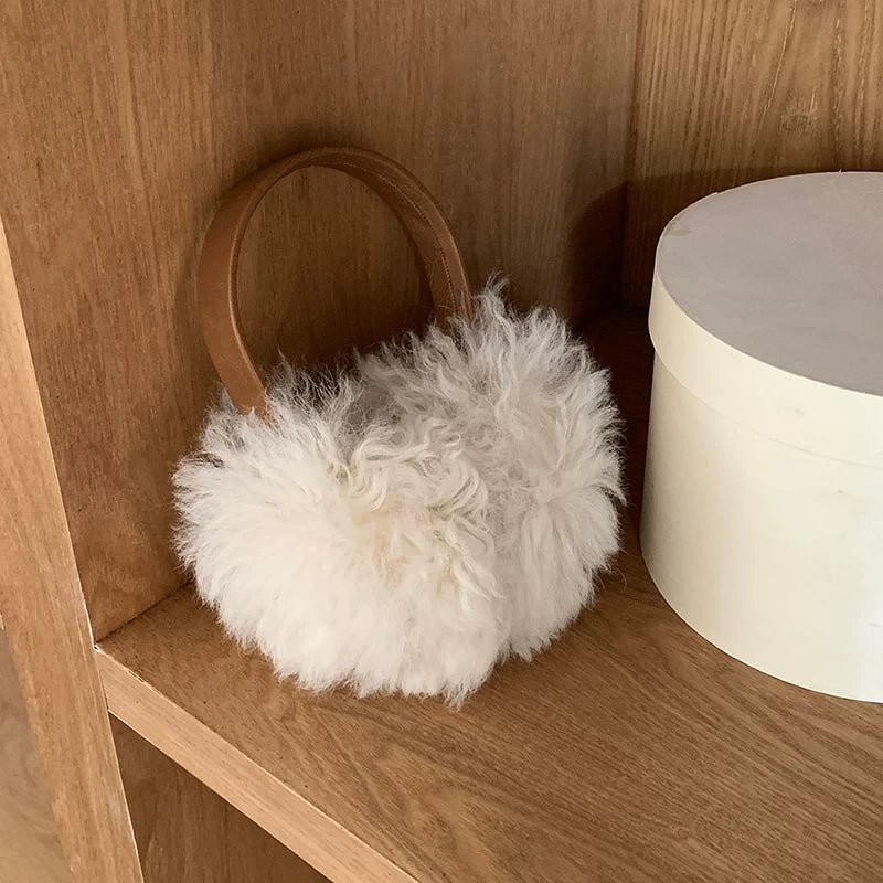 White wool earmuffs with a brown headband displayed on a wooden shelf