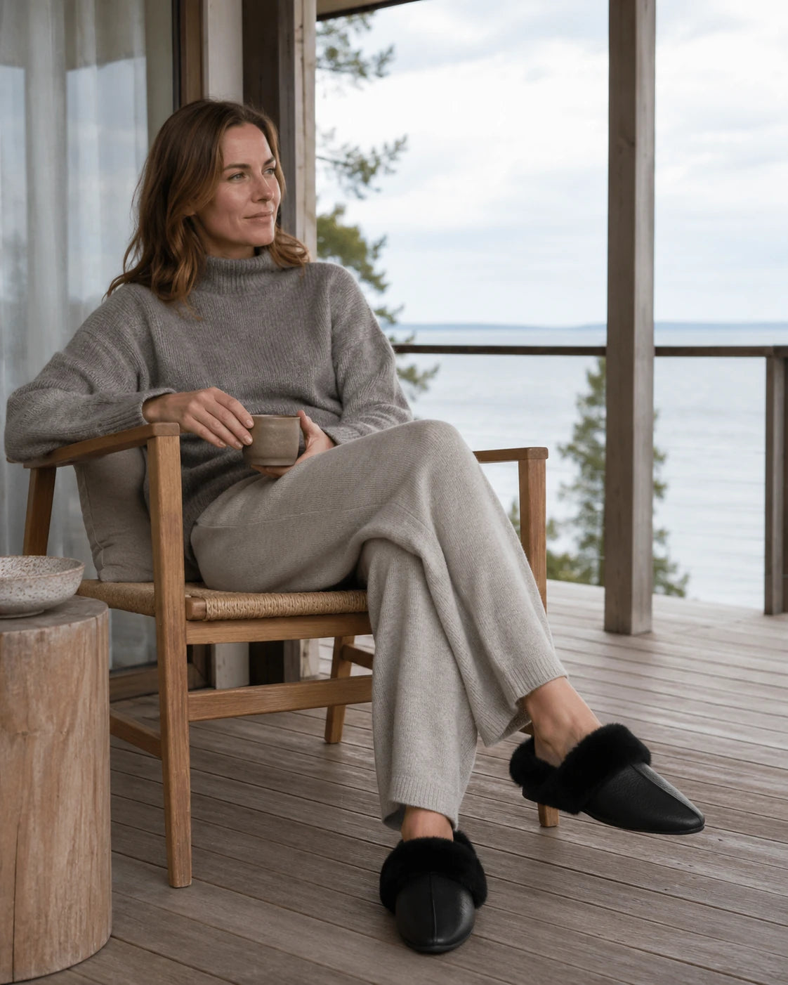 Woman seated by a window wearing black cowhide and rabbit fur mule slippers