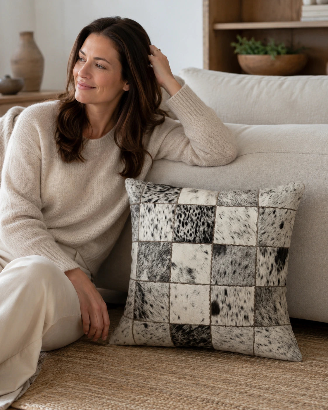 Woman relaxing on a neutral sofa with a black and ivory cowhide patchwork pillow