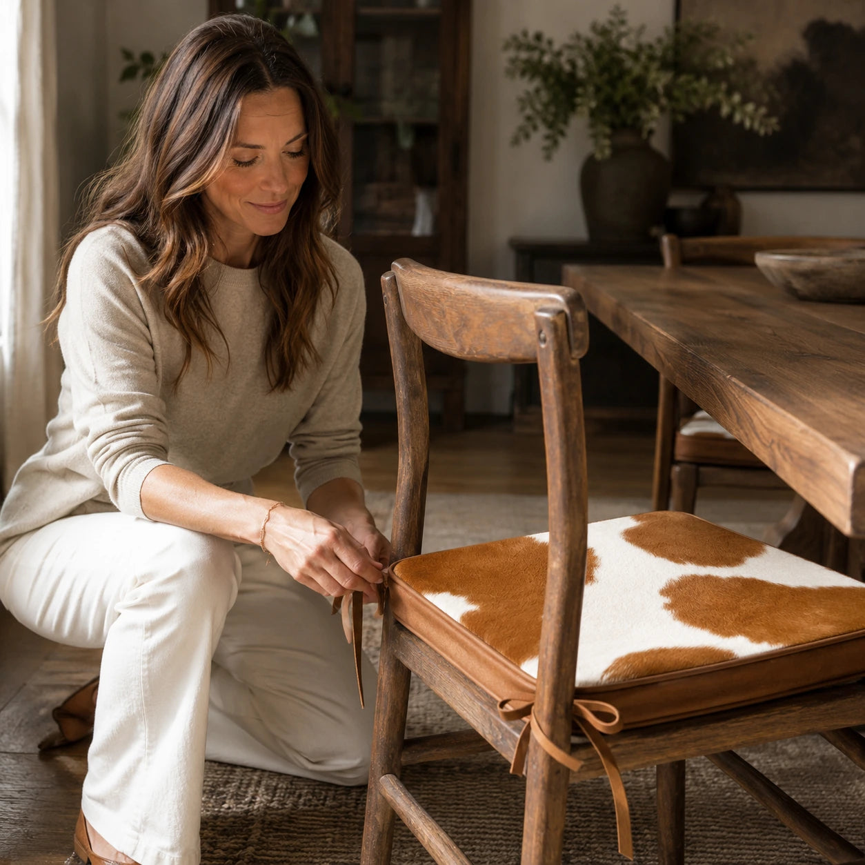 Woman securing a brown and ivory genuine cowhide chair pad to a wood dining chair