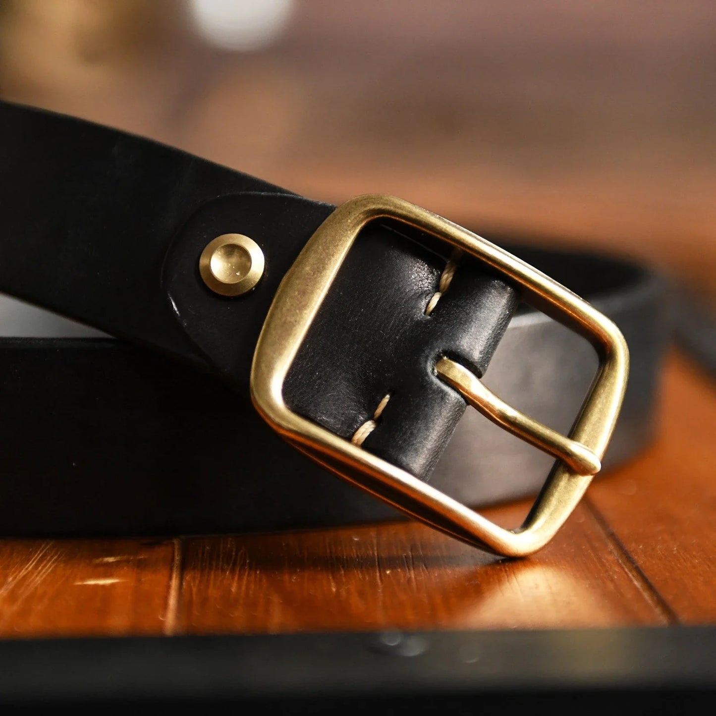 Black cowhide belt with aged brass-tone buckle closeup