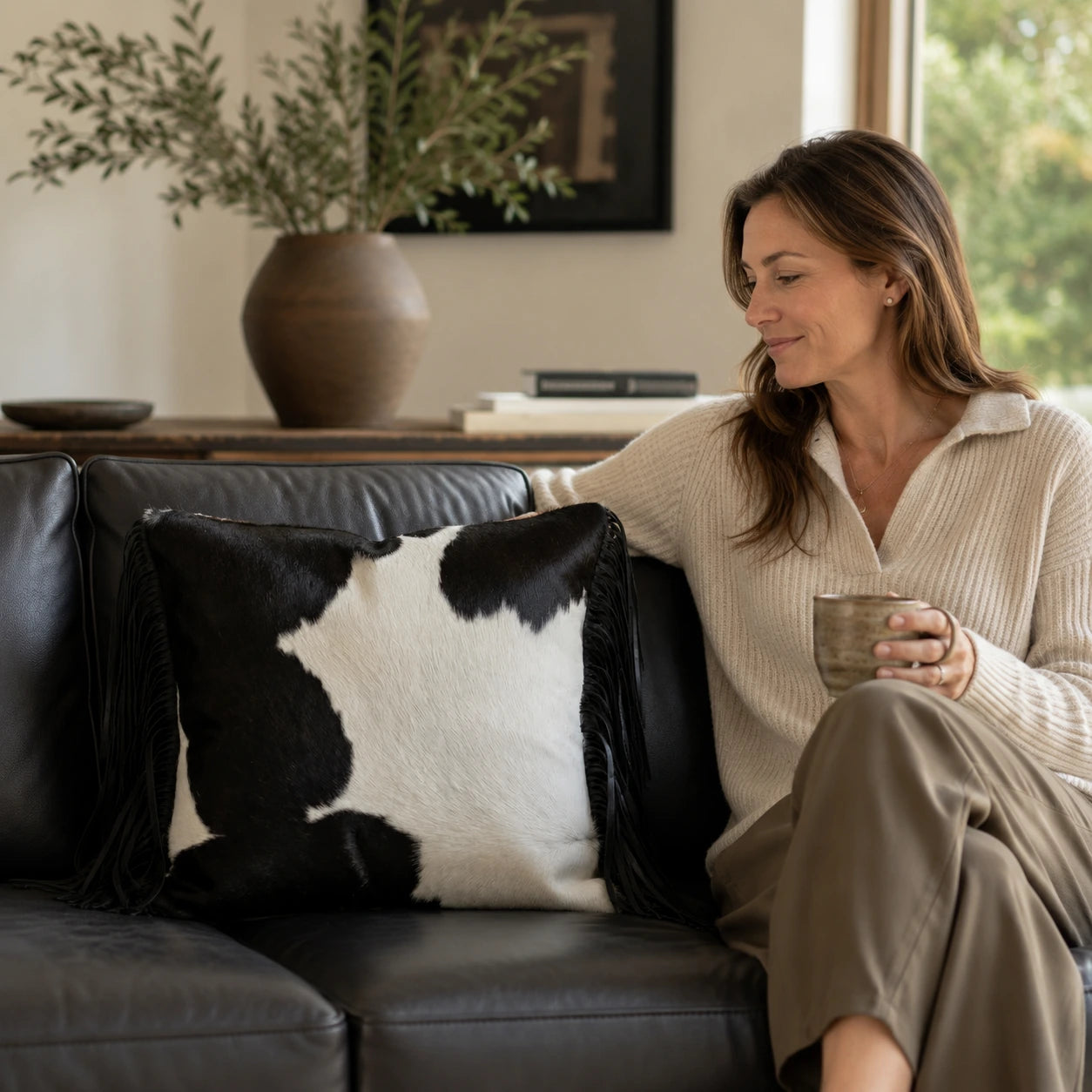 Woman relaxing beside a black and ivory fringed cowhide square pillow
