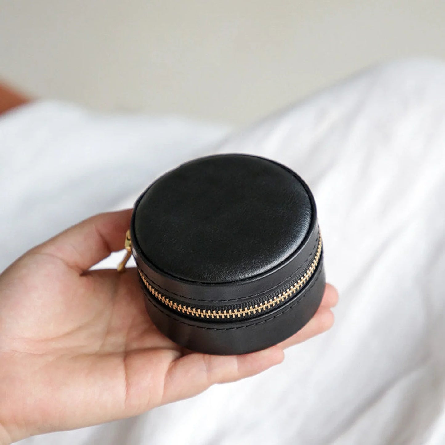 Black round leather travel jewelry case shown in hand