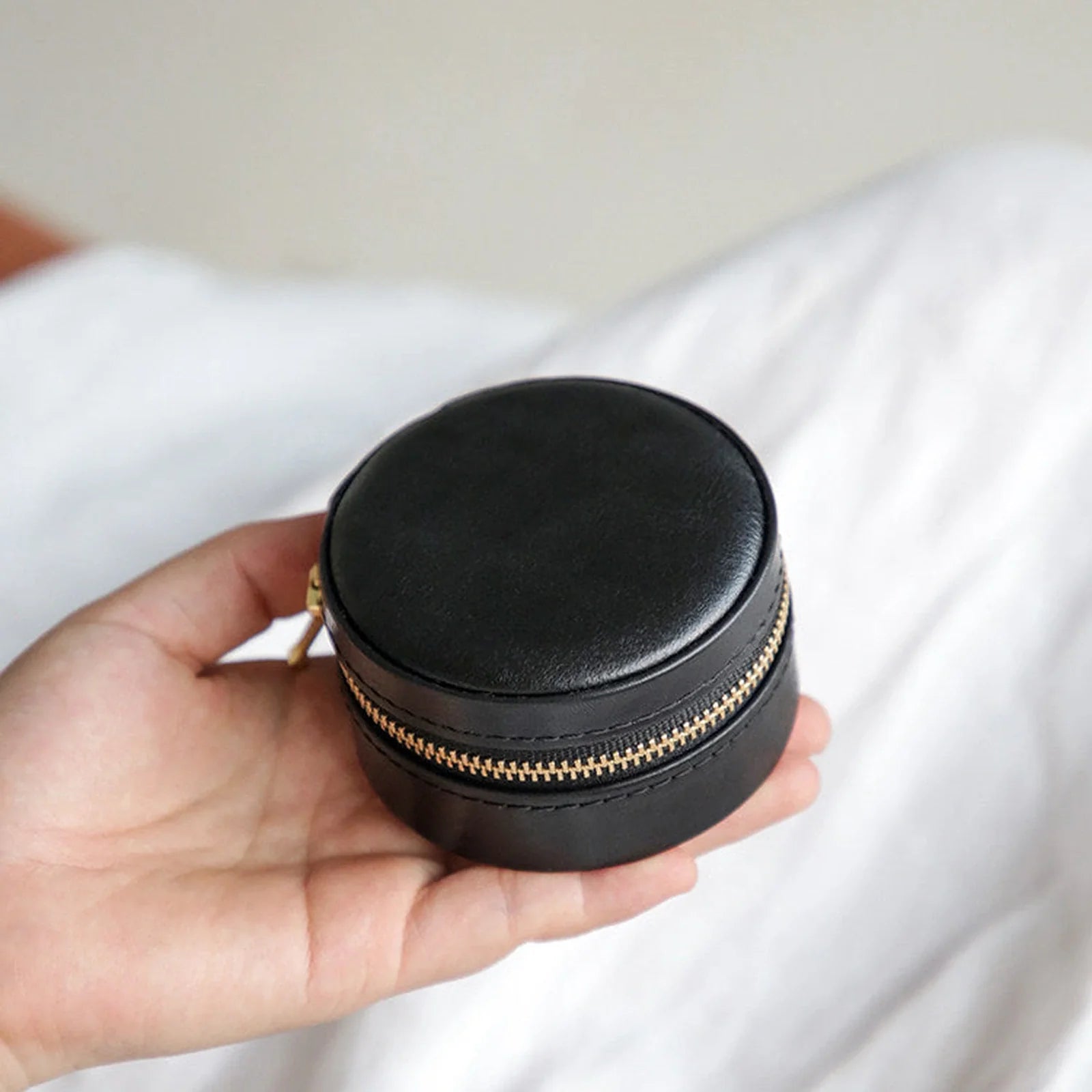 Black round leather travel jewelry case shown in hand