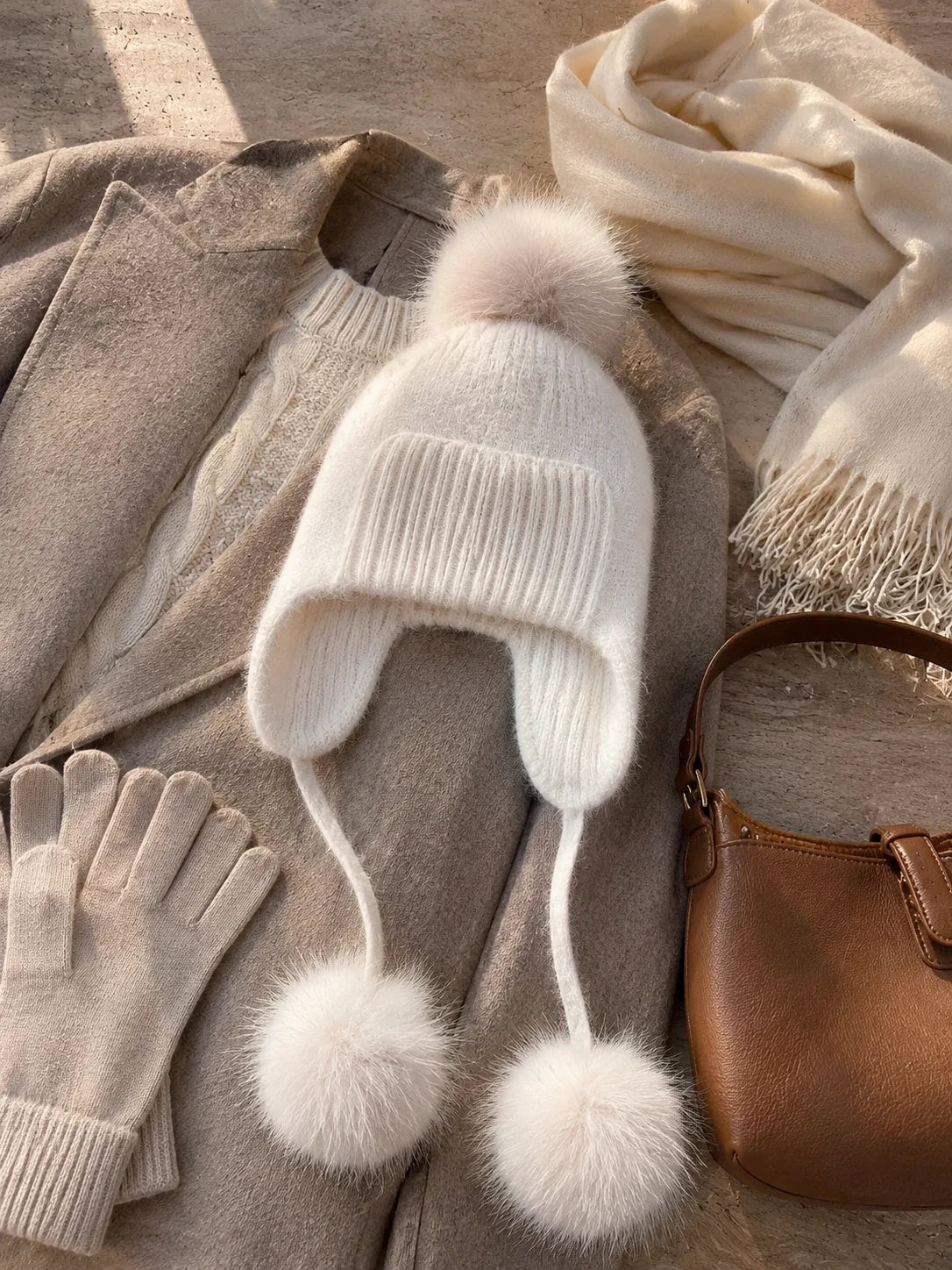 Knit earflap pom-pom hat styled with a coat, knitwear, gloves and a handbag